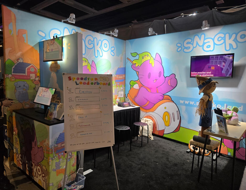Snacko&#39;s PAX West booth in 2024. I designed and worked with manufacturers to create a two-walled fabric print set up with Snacko&#39;s branding. The booth had four playable stations, a mirrored monitor for spectators, a leaderboard for attendees looking for a